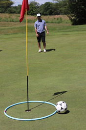 Man standing near a soccer ball and a golf flag at 2023 Golf Tournament.