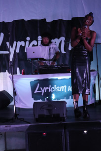 DJ and singer performing at a Lyricism UK event, with stage and banner background.