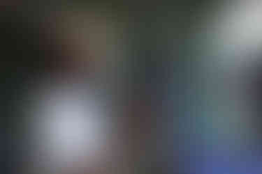 Man speaking into microphone, wearing sunglasses. Another man in the background.