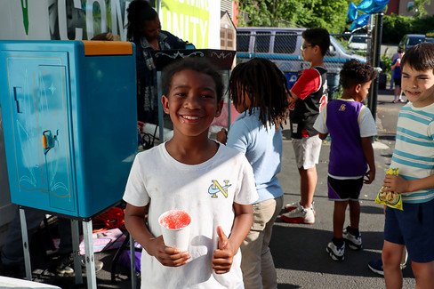 Smiling boy holds a drink giving a thumbs up, in an outdoor setting.