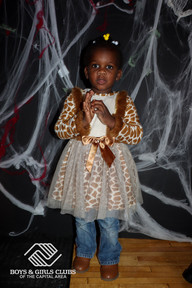 Young girl in giraffe Halloween costume stands against a spiderweb background BGCCA