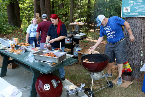 People grilling food at picnic with table and text. BGCCA