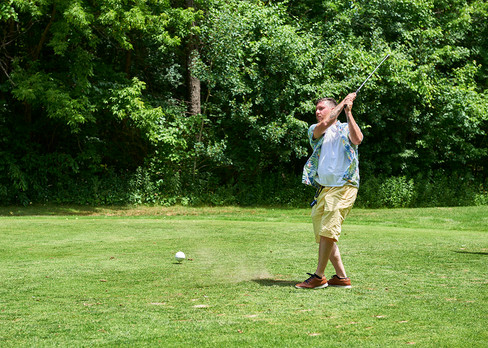 Man swinging golf club on course, ball mid-flight, green grass background