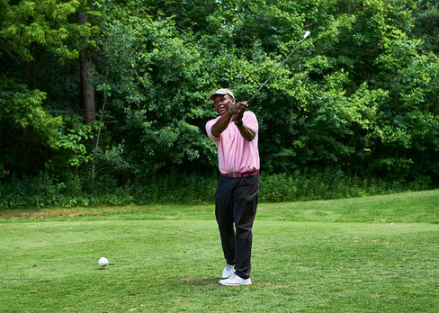 Golfer swinging a golf club on green grass with trees in the background
