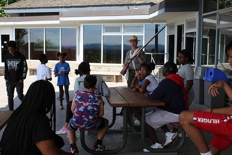 Group of kids with park ranger, outdoors, mountains in the background.