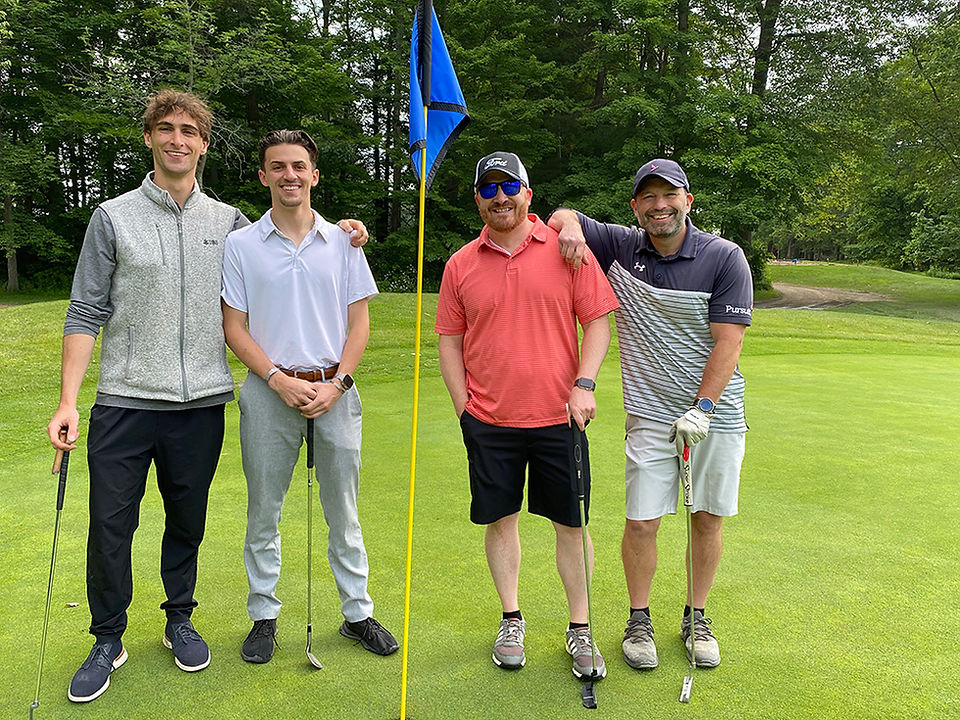 Four men on a golf course posed with clubs in the sunshine.