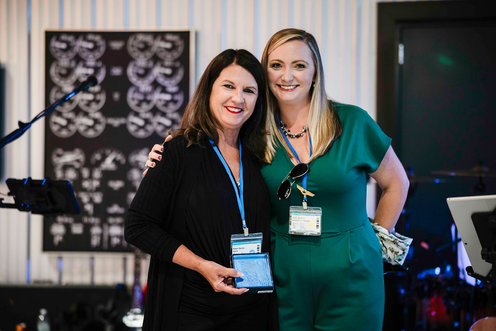 Two women smiling and posing together with badges at an event.