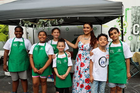 Group of children and woman in green aprons posing for photo.