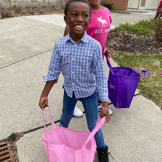 Smiling child holding pink bag, standing on pavement, near other person BGCCA.