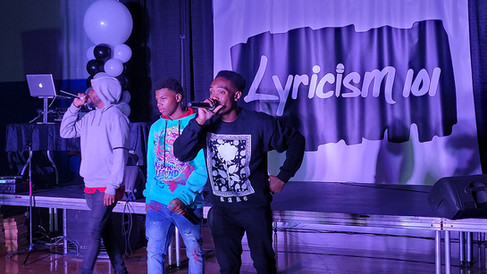 Two young men on stage performing with the word Lyricism in the background