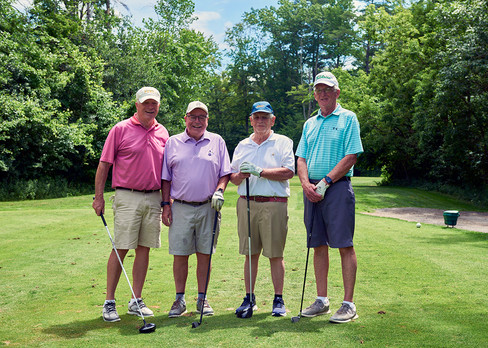Four men with golf clubs pose together on a sunny golf course.