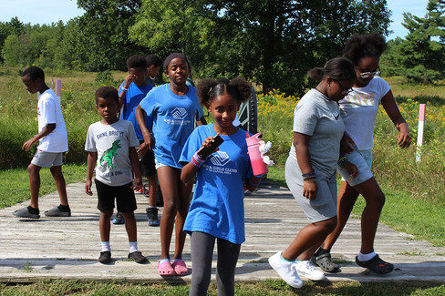 Group of kids wearing BGCCA shirts walking on a boardwalk outdoors.