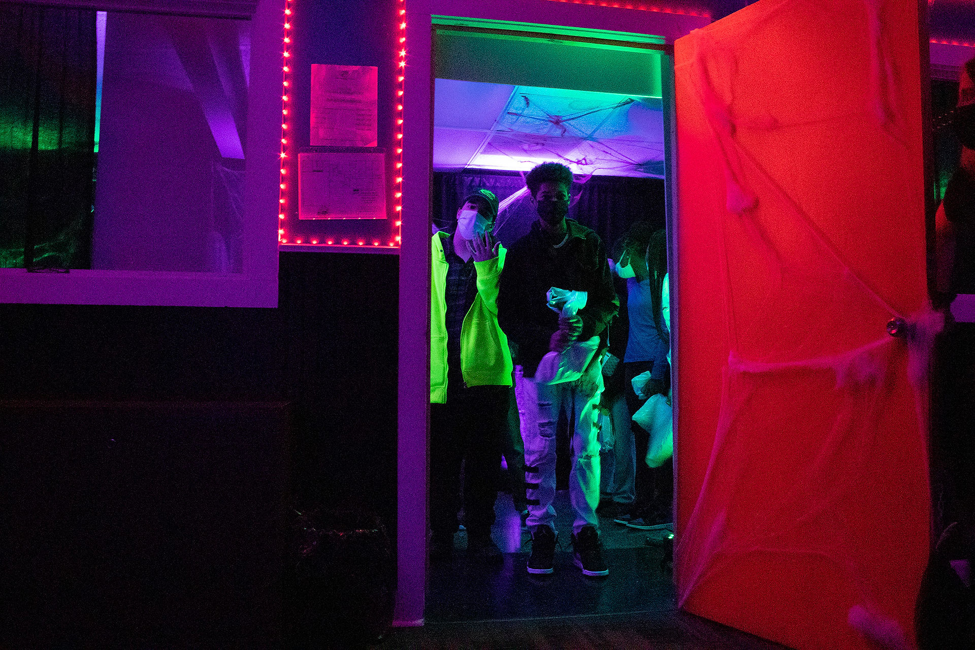 Man walking through a doorway in a neon-lit room BGCCA inside.