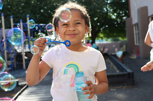 Young girl blowing bubbles smiling with a bubble wand outdoors on sunny day