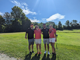 Four golfers posing together on the golf course with blue sky background