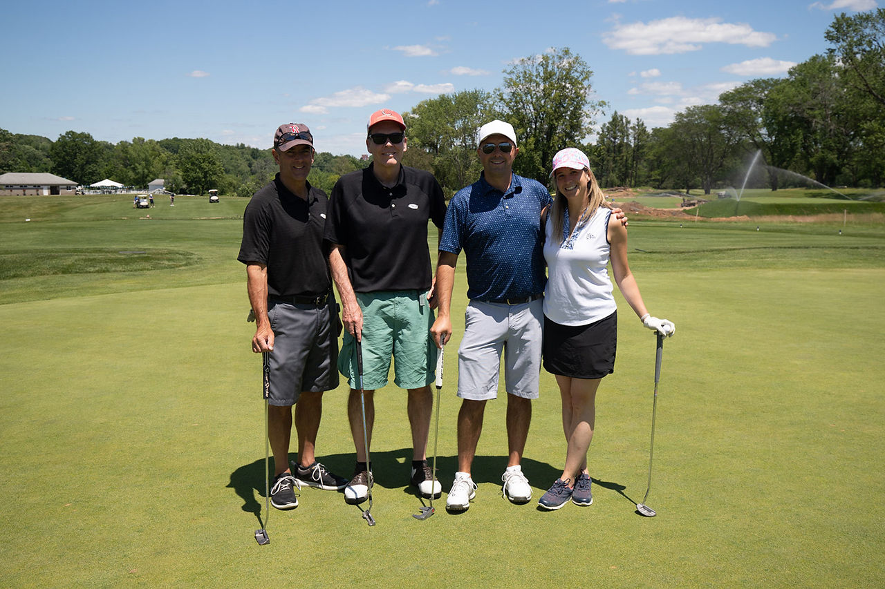 Four golfers smiling on a green golf course pose for photo, 2021 Chip In Fore Youth.