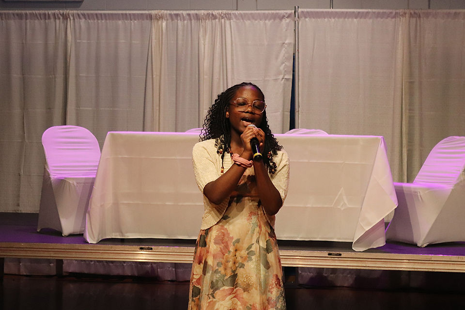 Woman with microphone speaking at an event, BGCCA presentation.