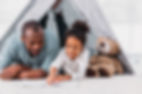 Father and daughter reading a book together inside a tent setting.