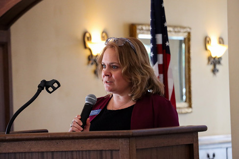 Woman speaking into microphone at podium; American flag in background. BGCCA