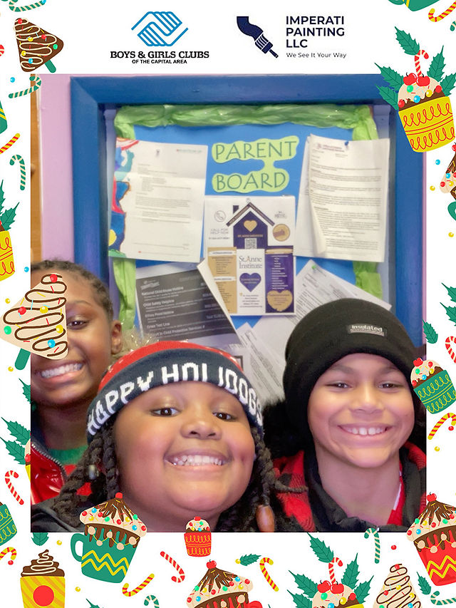 Three smiling children pose in front of a Parent Board with various papers.