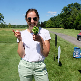 Smiling woman holding a plant on a sunny day at a golf course.