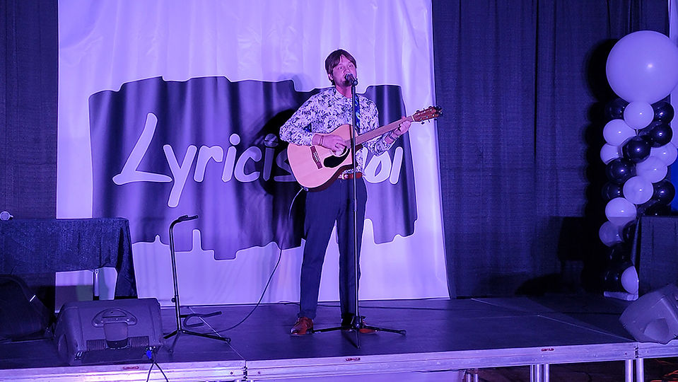 Man playing acoustic guitar on stage; Lyrical; Live music performance.