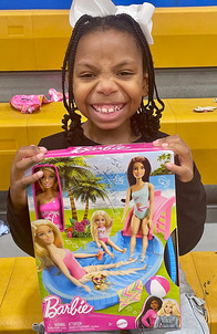 Young girl smiling with a Barbie playset, featuring dolls and pool.