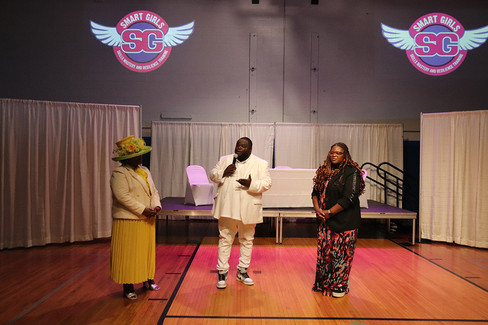 Three people standing on stage, Smart Girls logo background, speaking at event. BGCCA.