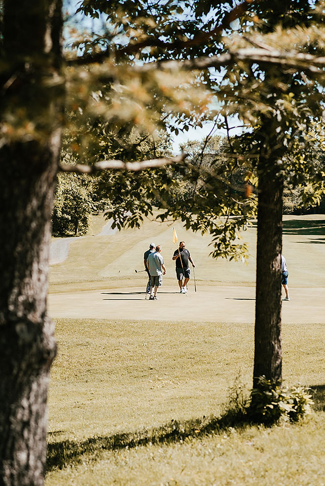 People walk on golf course in the distance near trees and foliage.
