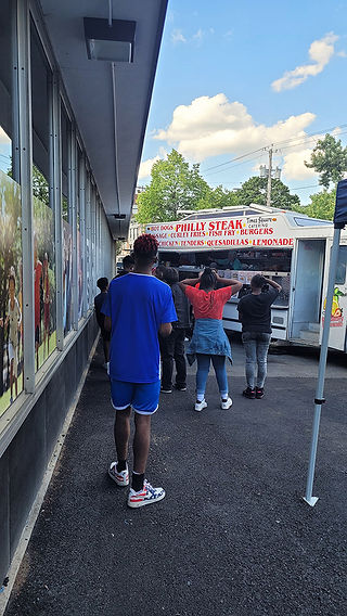 People line up at a food truck selling Philly steak, burgers, and lemonade.