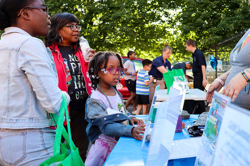 Girl looking at a display with others 2024-25 Kwanzaa BGCCA event with tables.