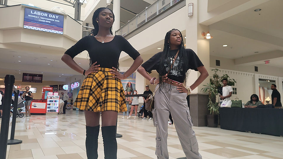 Two young women posing in a mall setting with arms akimbo fashion.