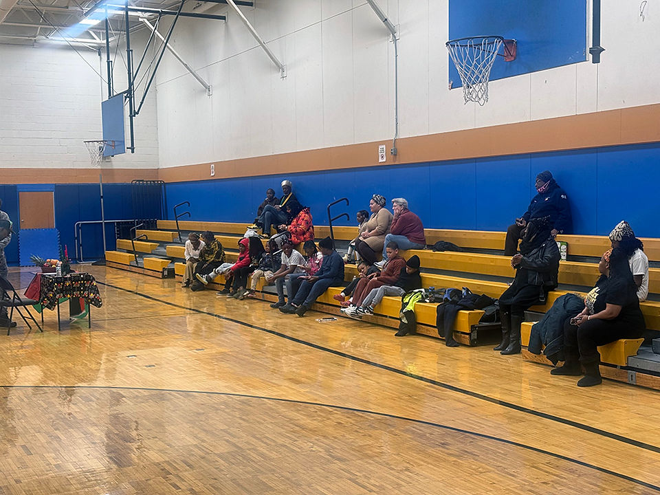 People seated on bleachers in a gym watching a basketball game at BGCCA.