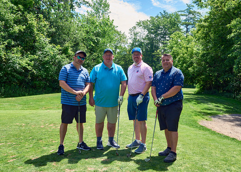 Four men posing with golf clubs, smiling and ready to play golf together.