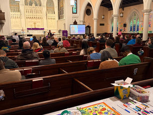 A congregation worshiping. Behind the pews is a table with a coloring station