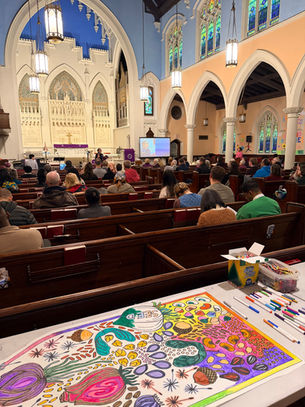 A congregation worshiping. Behind the pews is a table with a coloring station