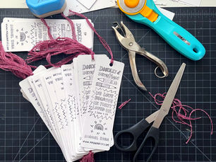 Pile of bookmars on a cutting mat, with scissors, rotary cutters, hole punchers, and thread