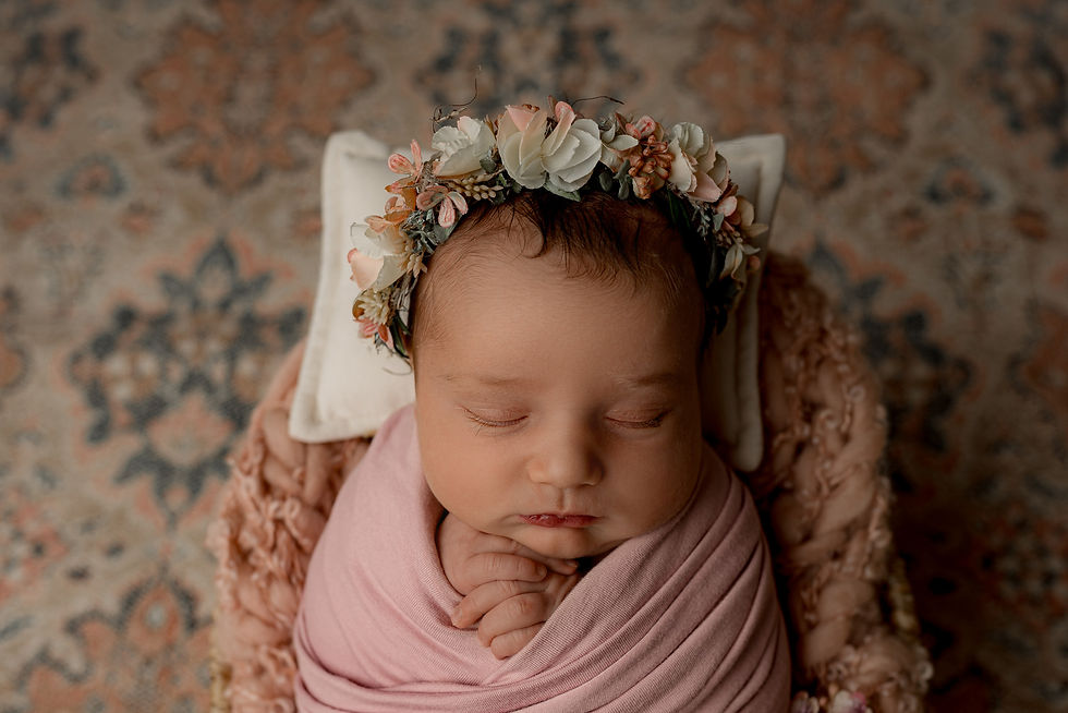 Neugeborenes schlafend, eingewickelt in ein rosa Tuch mit einem Blumenhaarkranz