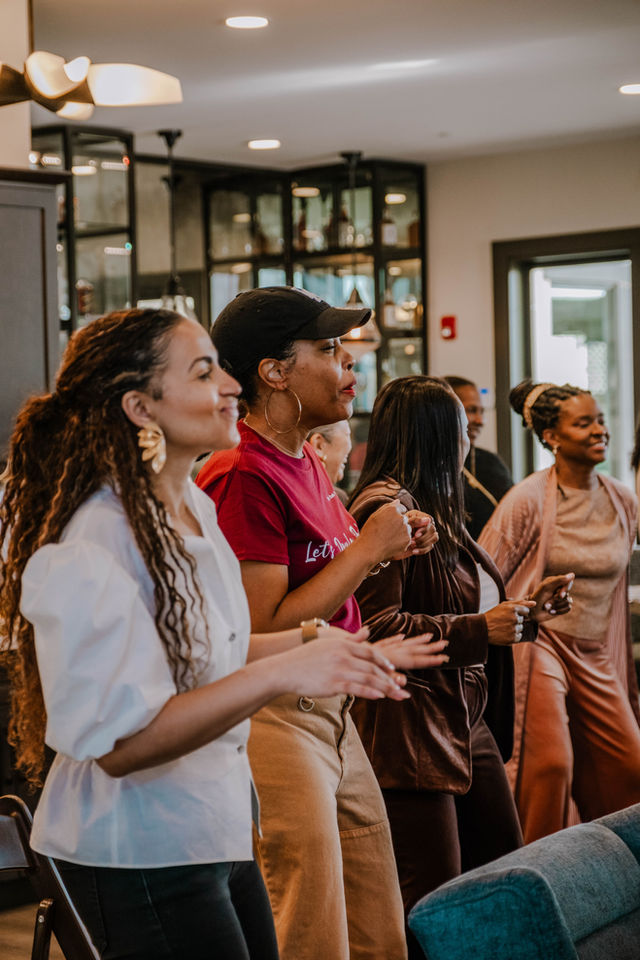 Group of women smiling and singing with their hands raised in The Doula Mansion