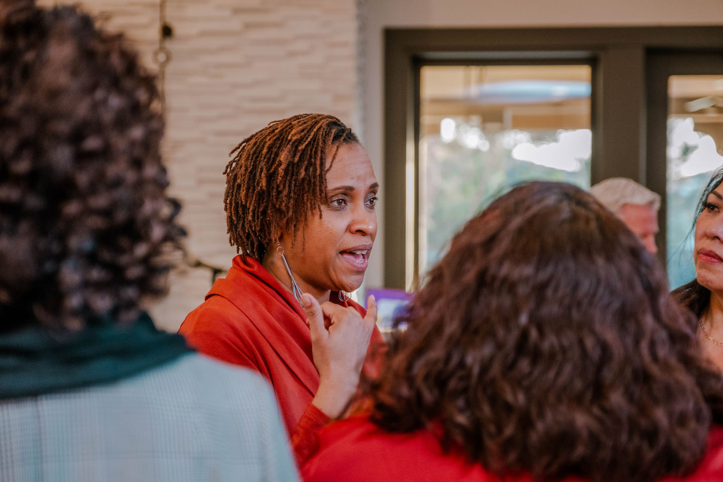 Woman speaking, surrounded by people, in The Doula Mansion. Engaging discussion taking place.