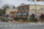 Small-town street scene with brick buildings, green awnings, and holiday wreaths.
