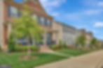 Row of suburban houses with brick and siding exteriors, manicured lawns, and colorful gardens under a clear blue sky.