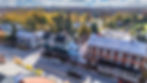 Aerial view of a small town street with colorful historic buildings, autumn trees in the background.