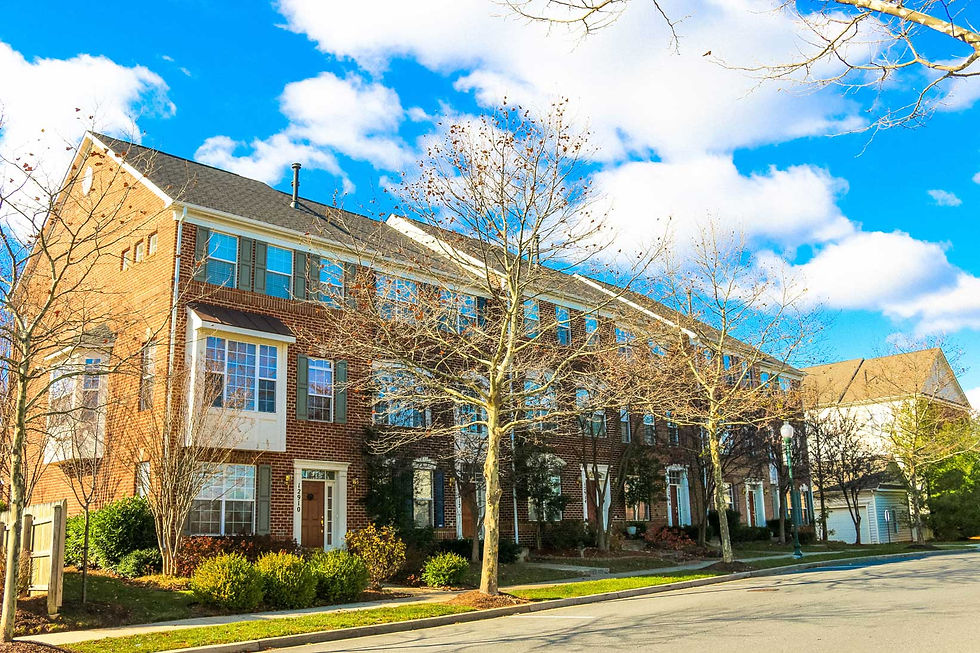 Brick townhouses with large windows under a bright blue sky. Leafless trees line the sidewalk. Calm suburban street scene.