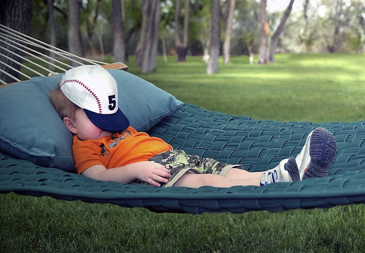 A young boy peacefully enjoys a nap in a hammock under the sun, his baseball cap carefully shielding his face.