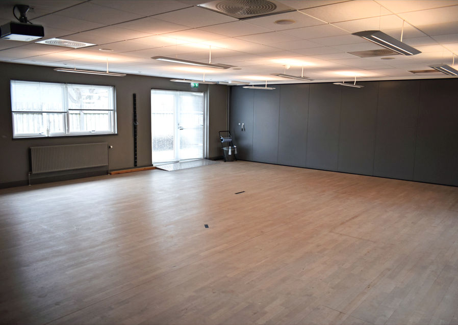 Træningssal med lyst trægulv og store vinduer