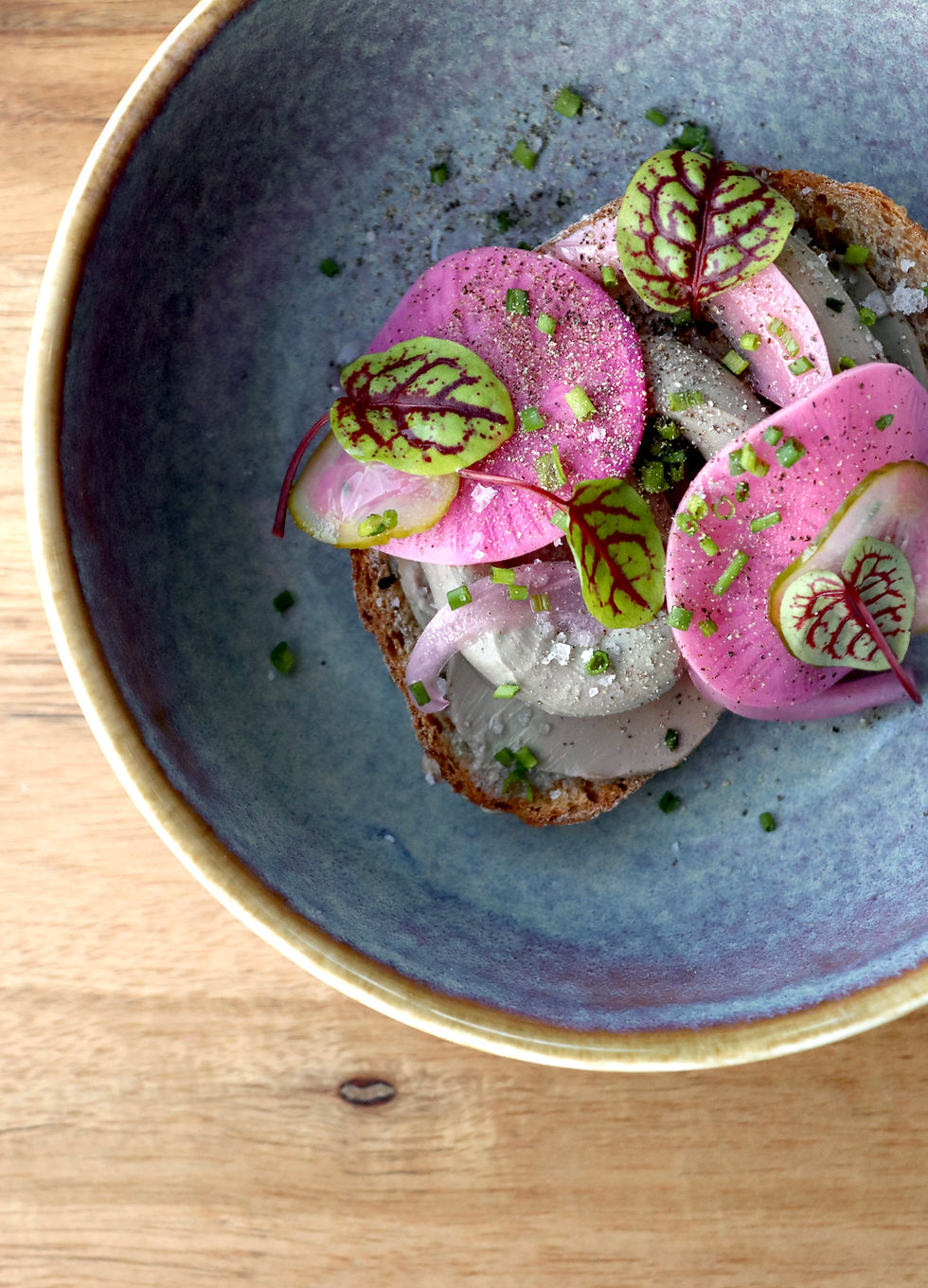 Toast with pink radishes in a speckled ceramic bowl