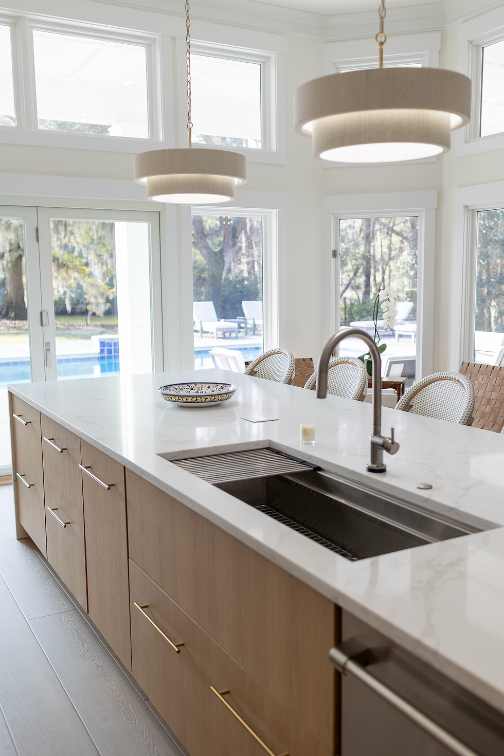 Bright modern kitchen with wood island, white counters, pendant lights, and a sink overlooking a sunny pool.