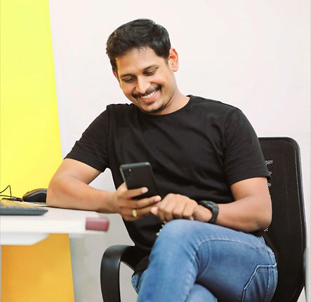Sai Ganesh, Founder and CEO of Sree Creative, sitting and smiling while using a phone