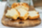 Gesneden cakebrood op een houten snijplank, met goudbruine korst en kruimels op de witte tafel.
